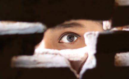 A mysterious eye peeks through a small gap in a brick wall, creating an intriguing and intense visual.